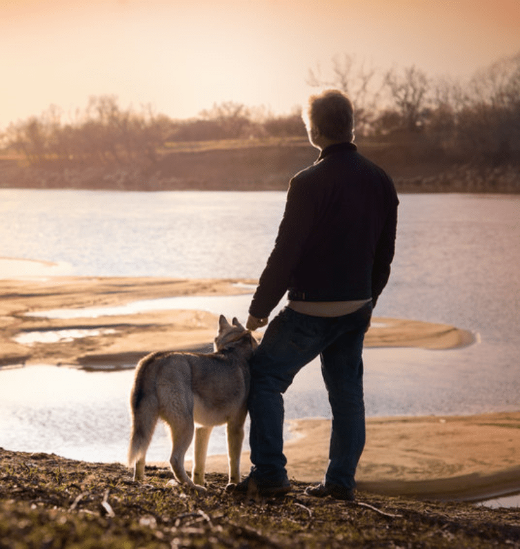 man and his dog standing by a lake