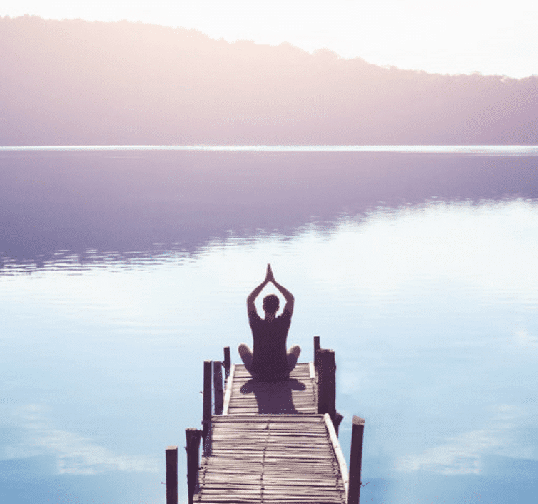 man practicing meditation on a dock at a lake in the mountains