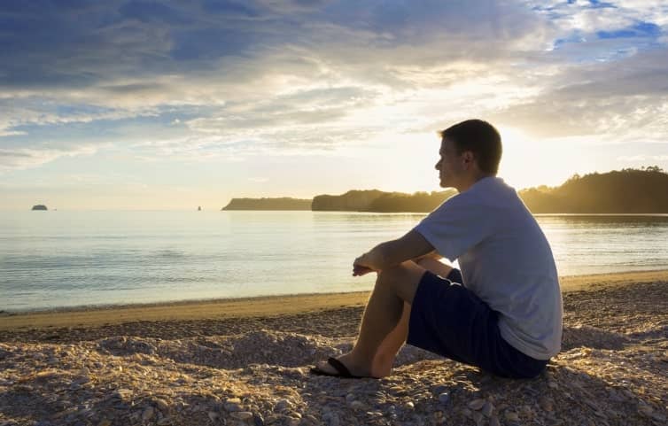 man sitting on beach staring into the water