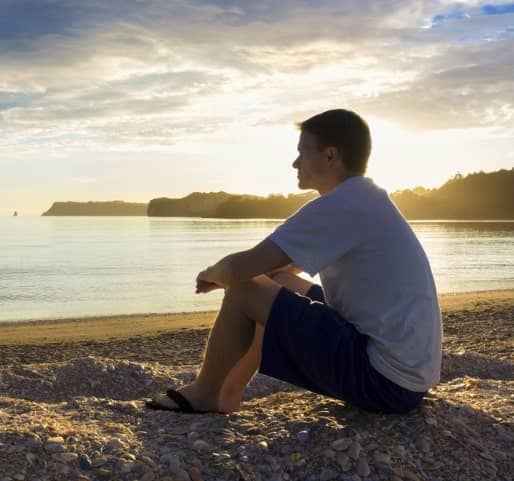 man sitting on beach staring at the water