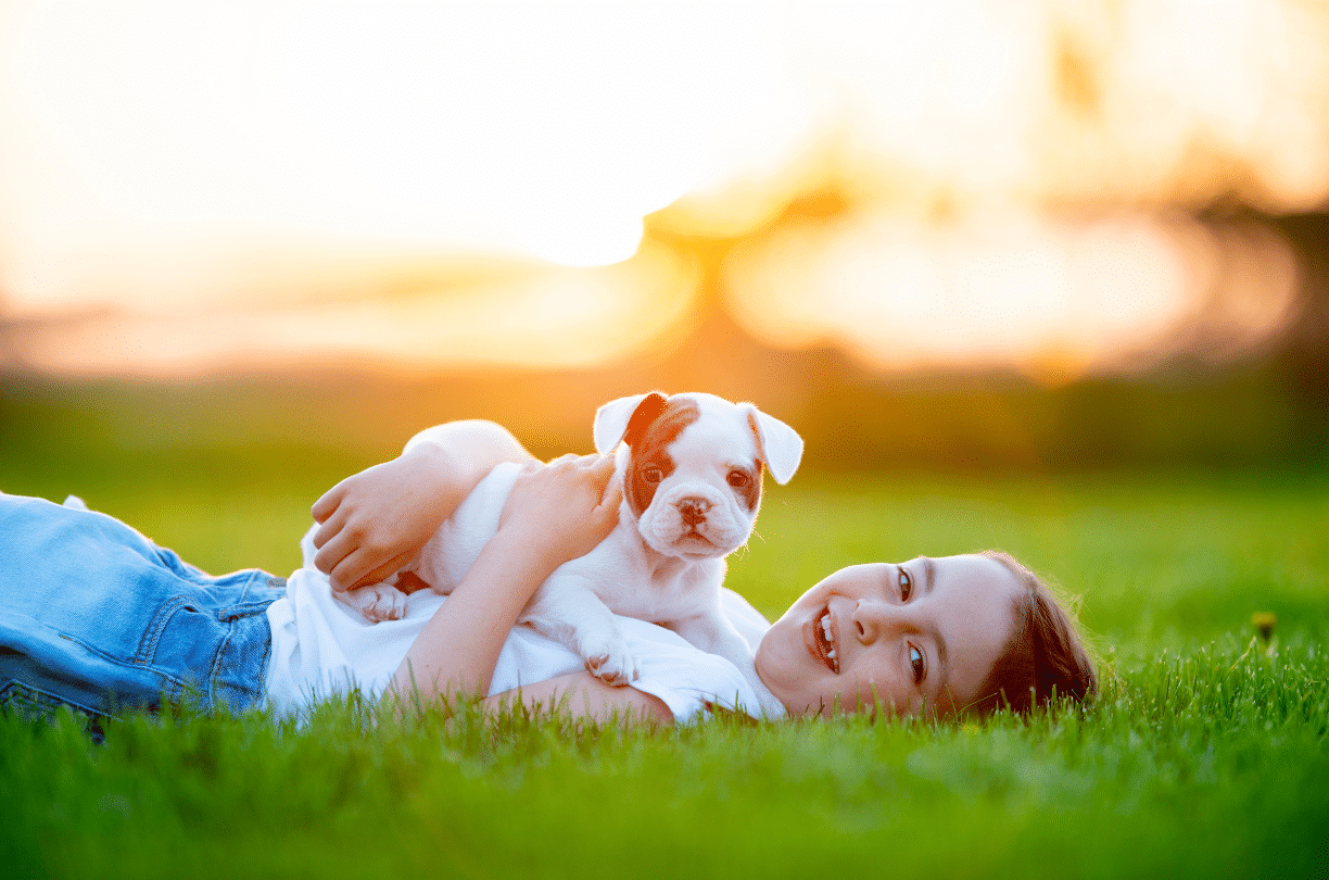 little girl laying on grass with a puppy on her