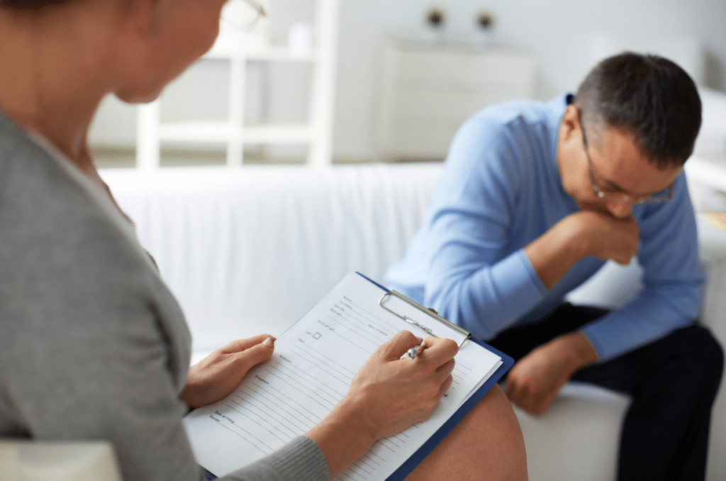 distressed man with head down talking to therapist while he takes notes