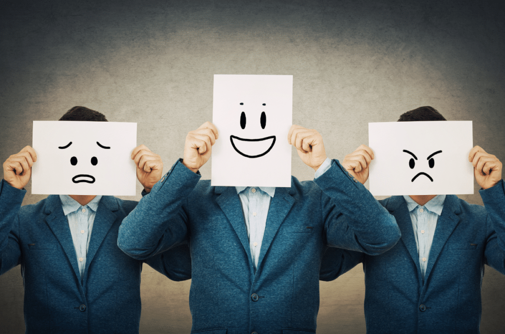 three men holding paper up to their face with different facial expressions on it