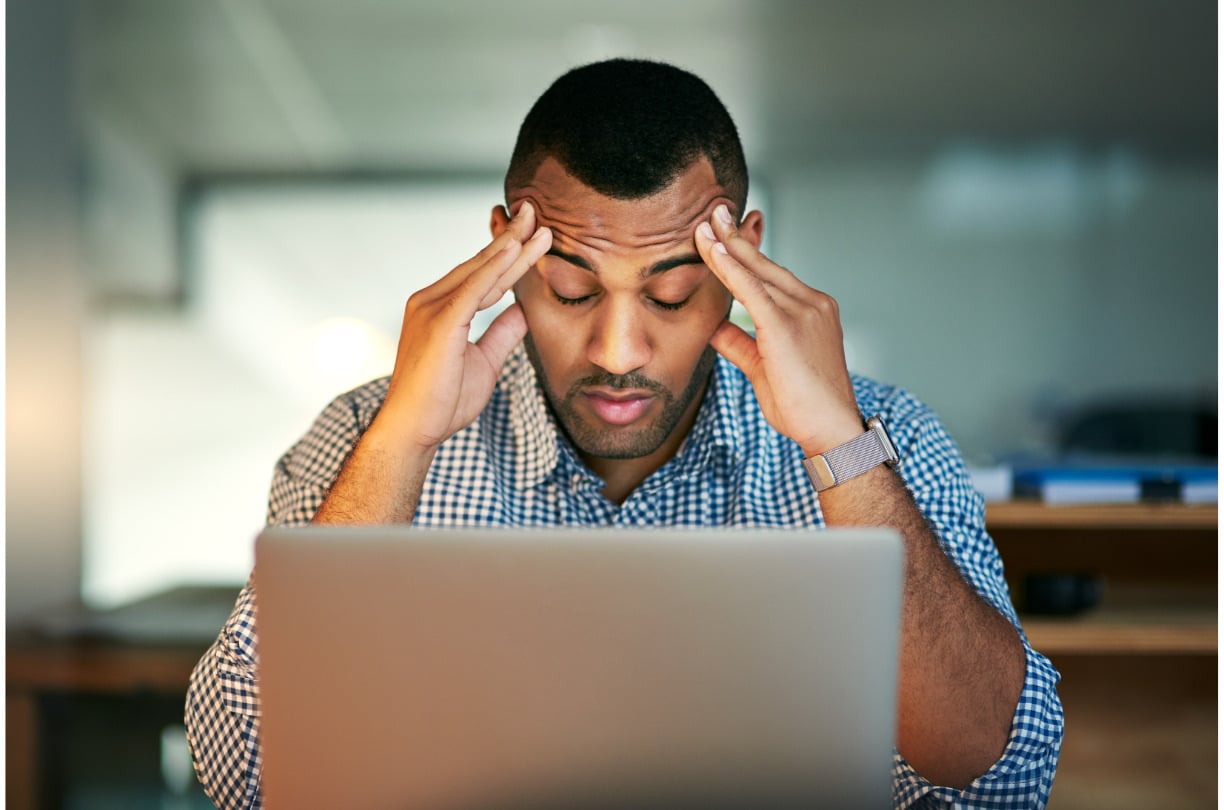 stressed man looking at computer with hands on temples of head