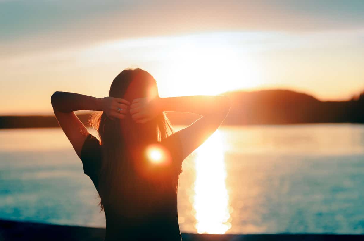 woman stretching arms on lake during sunrise