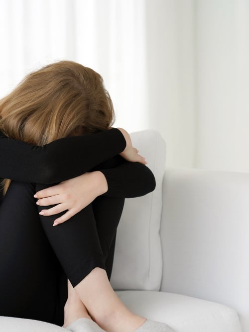 woman hugging knees crying on couch