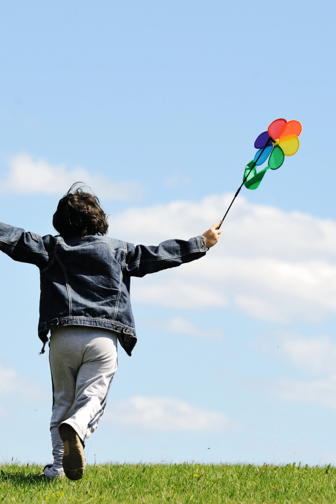 little boy running in grass with a toy windmill