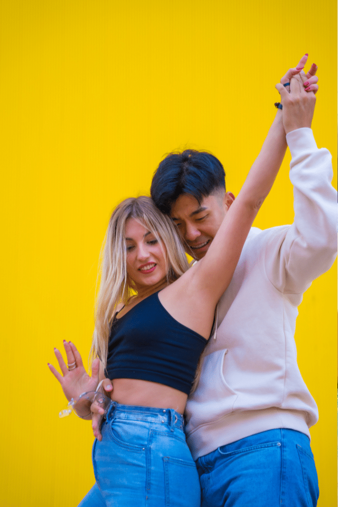 man and a woman dancing together in front of a yellow wall