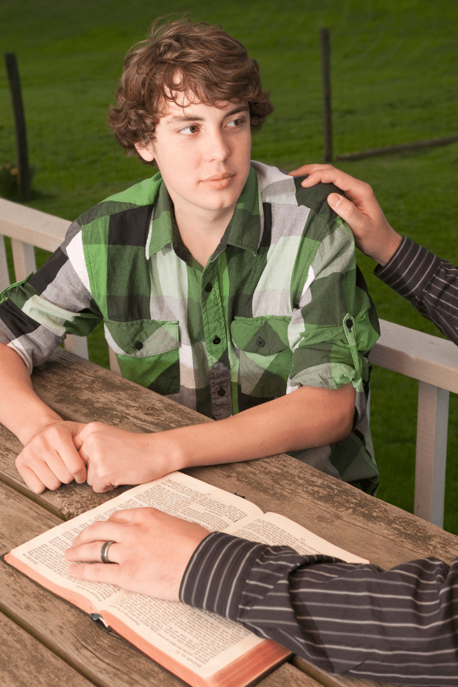 man holding open the bible and talking to his teenager outside about problems