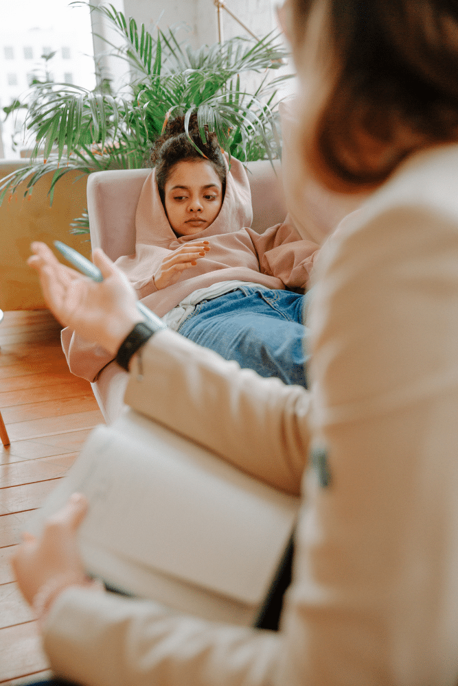 depressed teenage girl laying on a couch in therapy while talking to a therapist