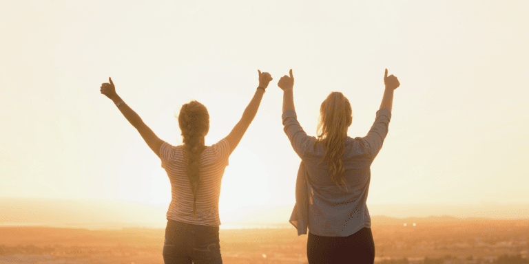 two women holding their thumbs up as they enjoy the view outside