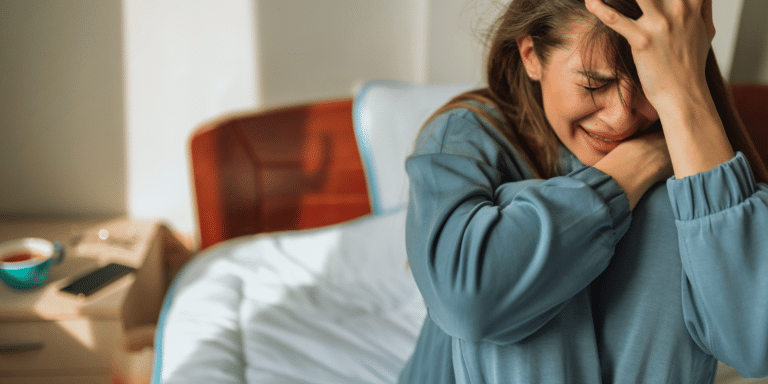 woman gripping her head in distress as she cries on her bed