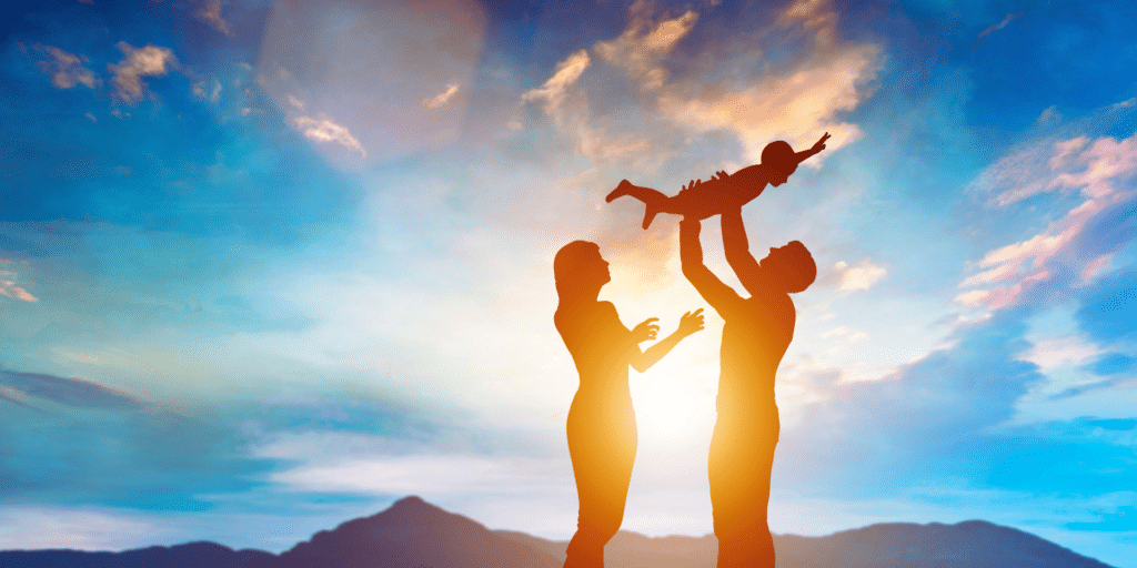 parents tossing their child up in the sky with joy, mountains as the background