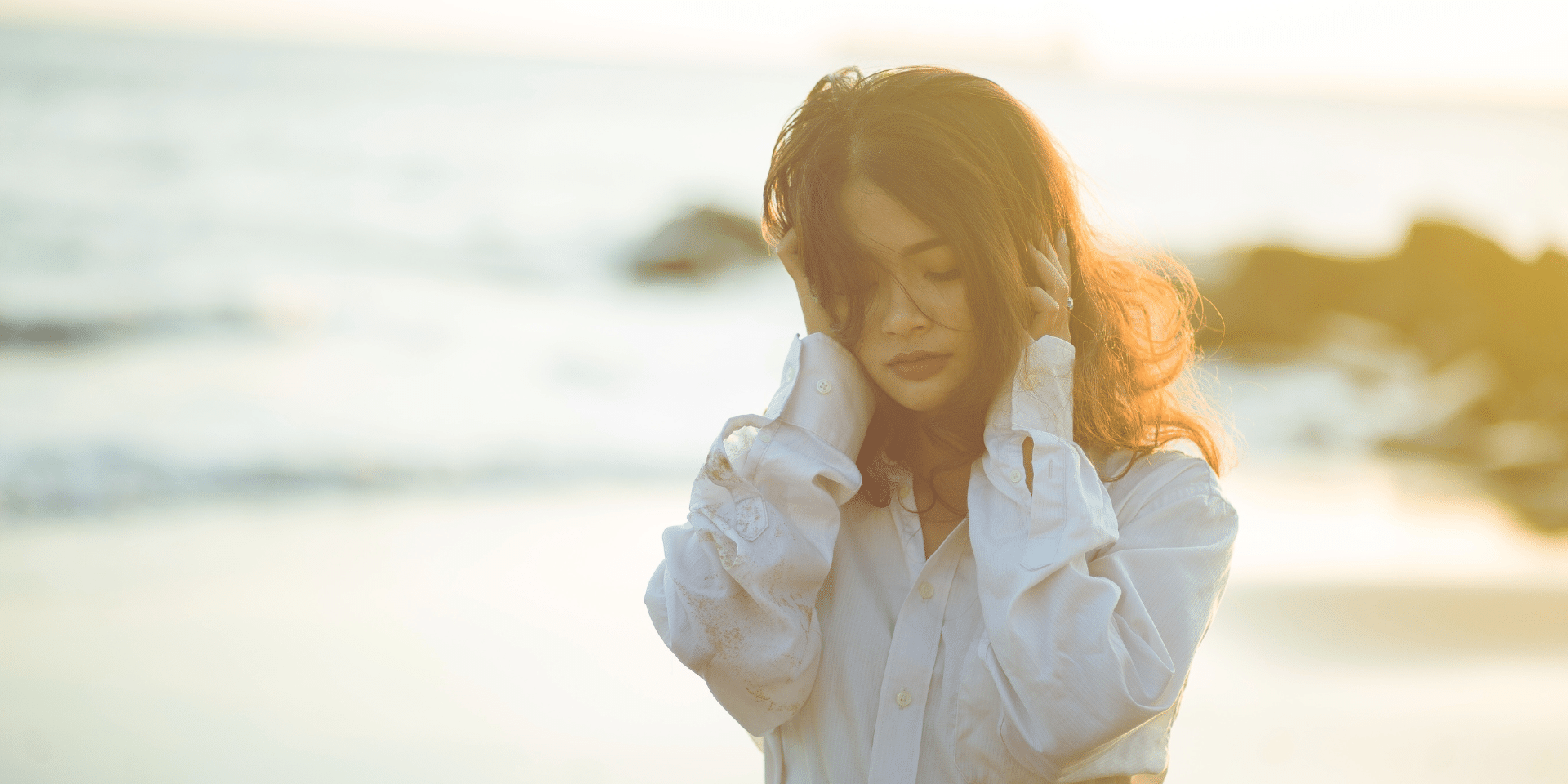 woman overwhelmed grabbing her head while outside on the beach, in need of therapy