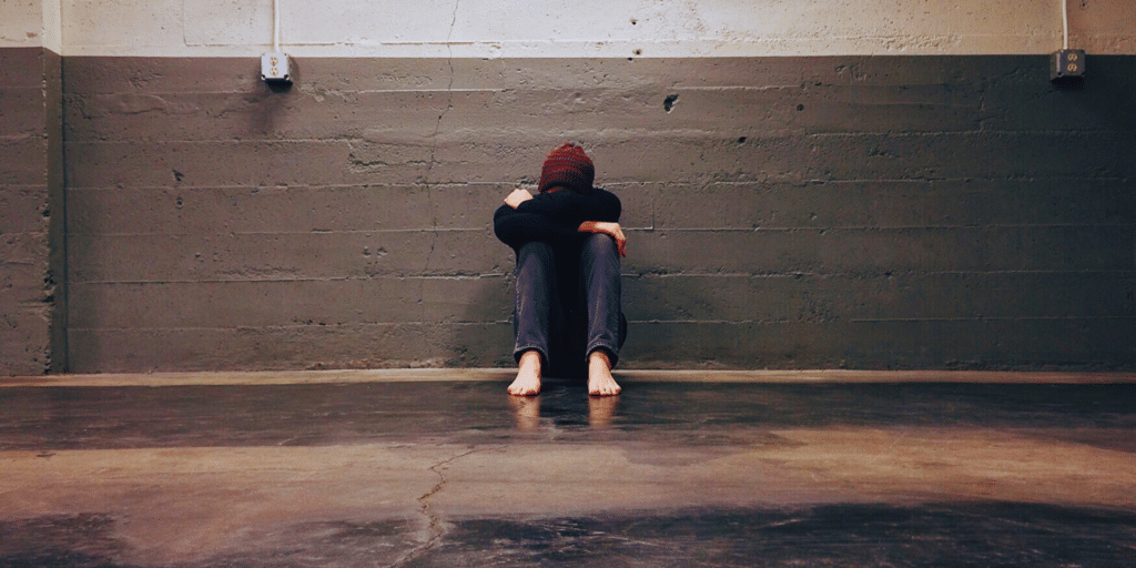 sad man holding his knees to his head and crying with his head looking down. outside sitting barefoot on concrete