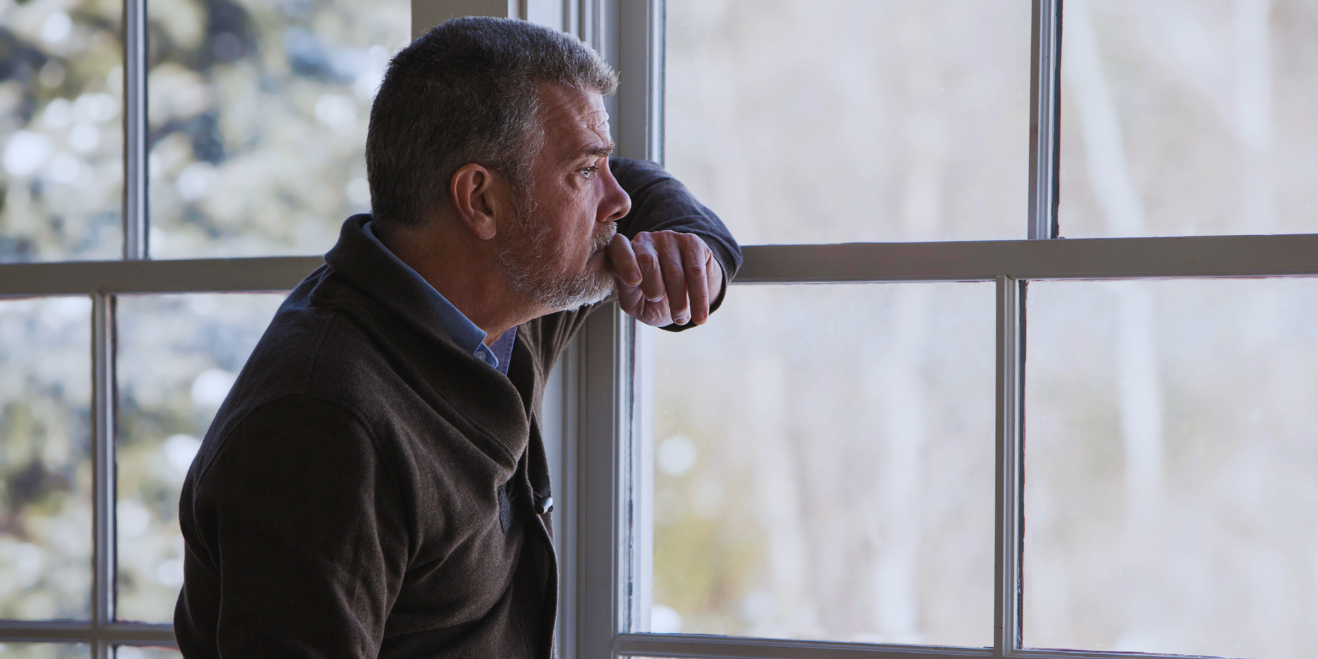 sad old man looking out a window and thinking. he looks distraught and upset