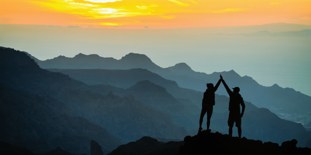 two people at sunrise high-fiving one another to represent support and accomplishment