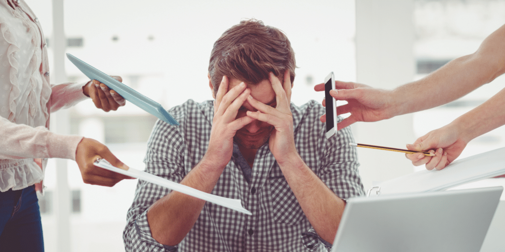 man feeling overwhelmed and stressed with a bunch of phones and paper being handed to him to symbolize over work, stress, and need to relax