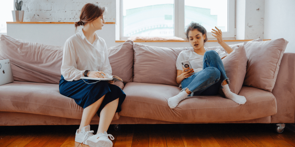 teenage girl sitting on the couch talking to her female therapist about issues she is having
