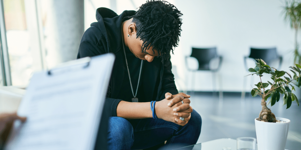 man in a therapy session holding his hands together and looking down symbolizing thinking or prayer