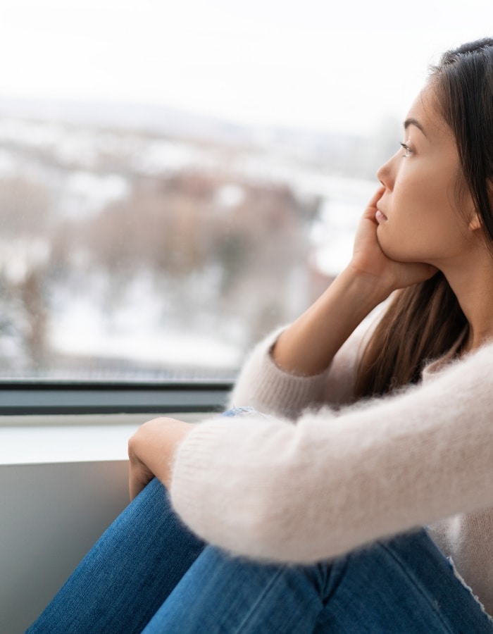 Young Asian woman gazing sadly out a window, representing depression and anxiety therapy in Denver