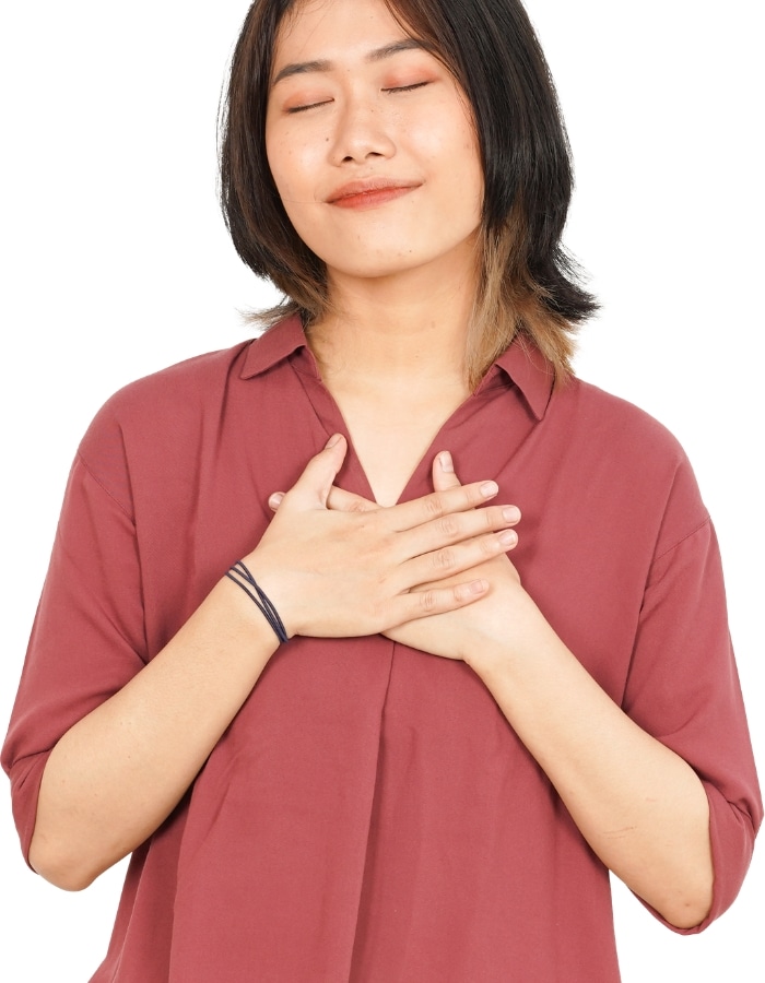 Asian woman with eyes closed and hands on her heart, representing self-compassion and mindfulness therapy