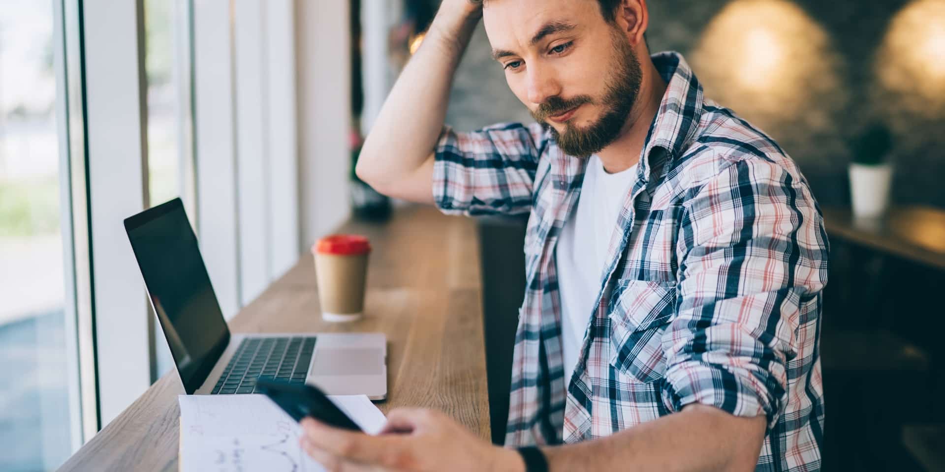 Man anxiously checking his phone at his laptop, representing high-functioning anxiety and work stress