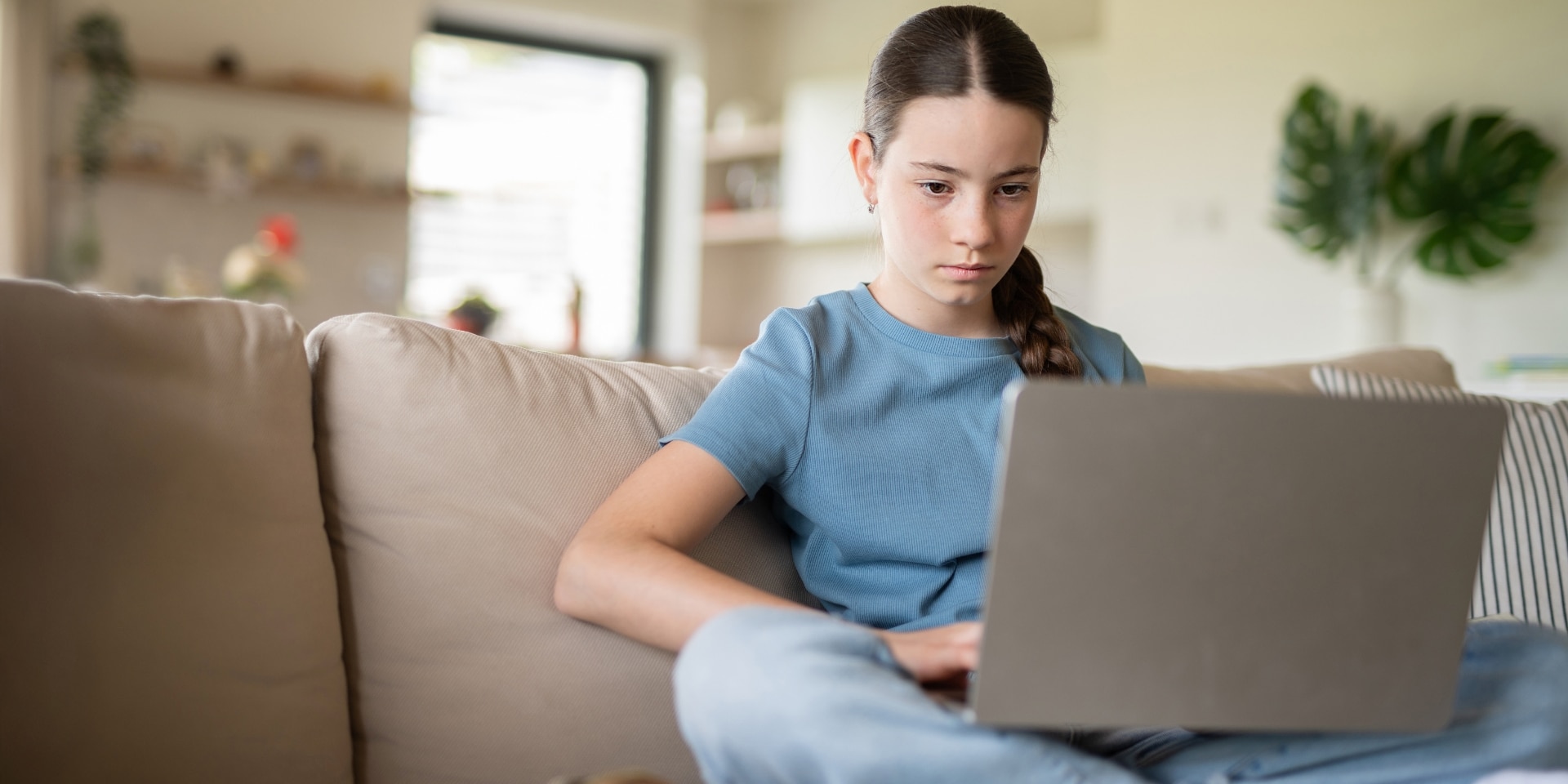 Teen girl focused on her laptop on the couch, representing academic pressure and teen anxiety therapy