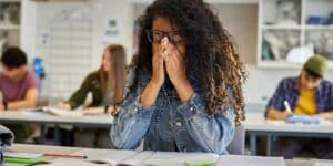 Stressed student covering her face with her hands in a classroom