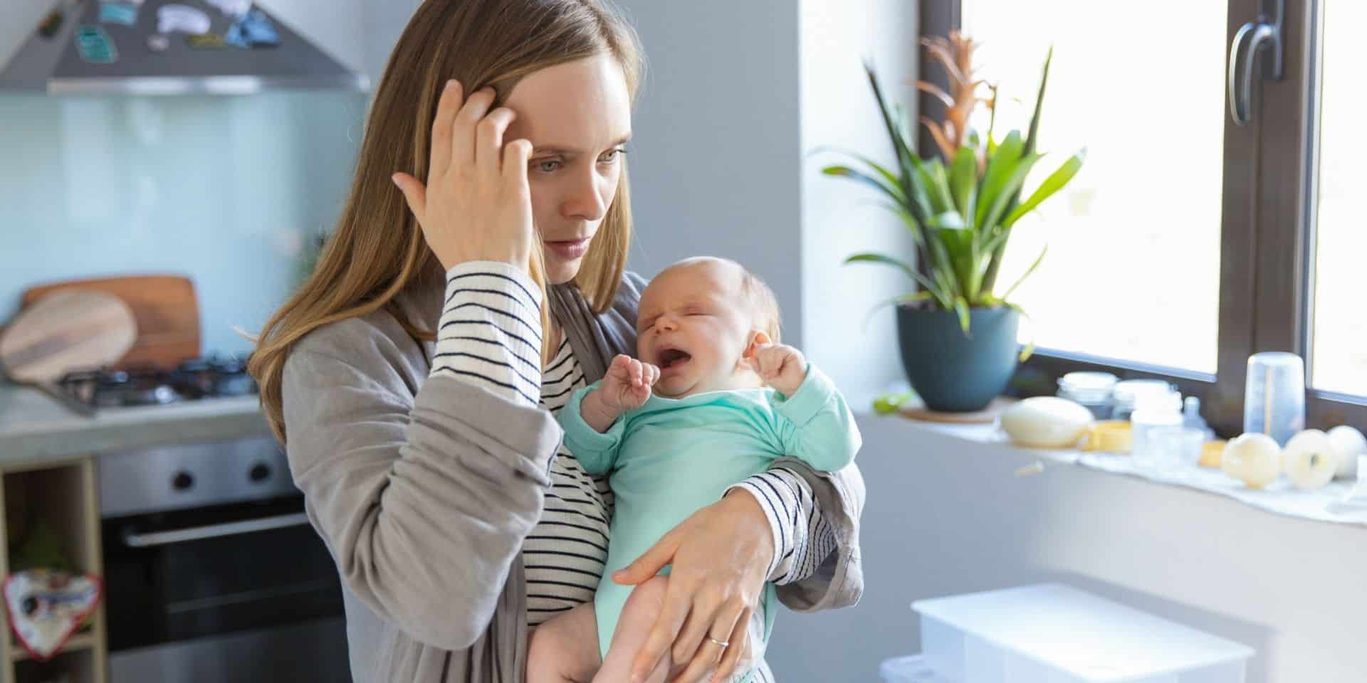 Tired new mother holding her crying baby in the kitchen