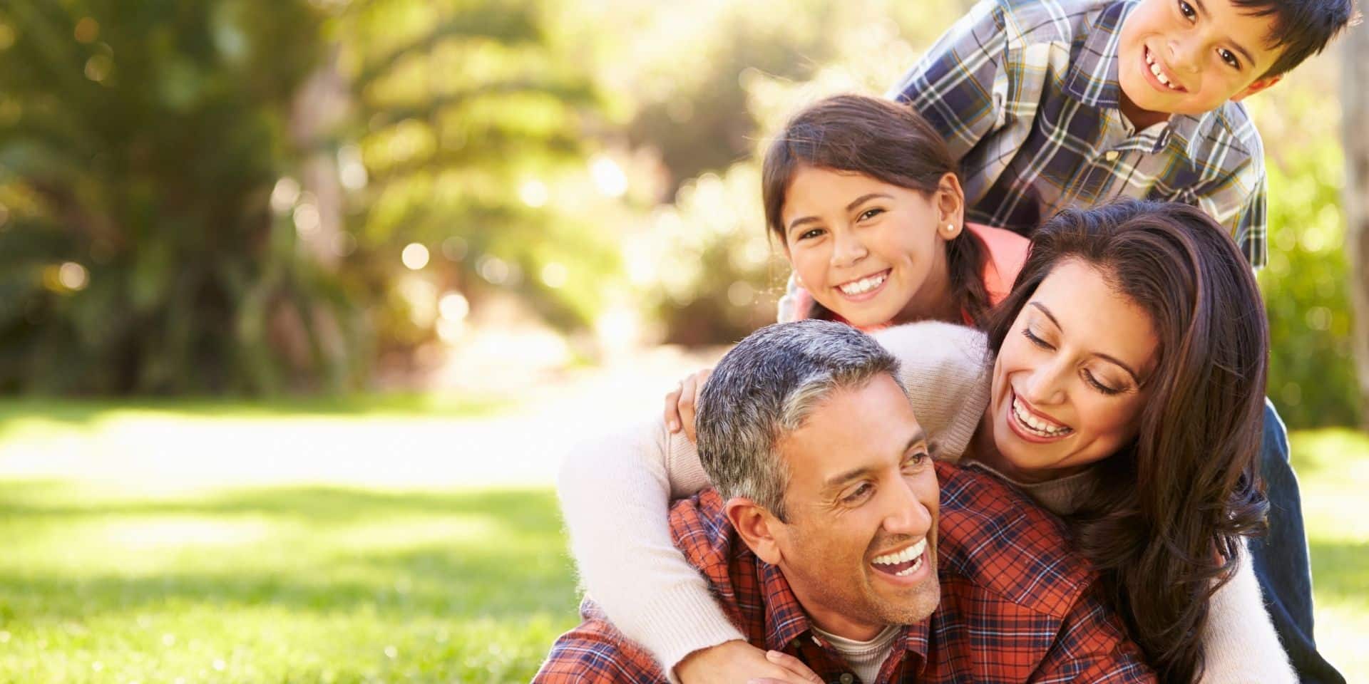 Smiling Hispanic family of four hugging outdoors in a sunny park