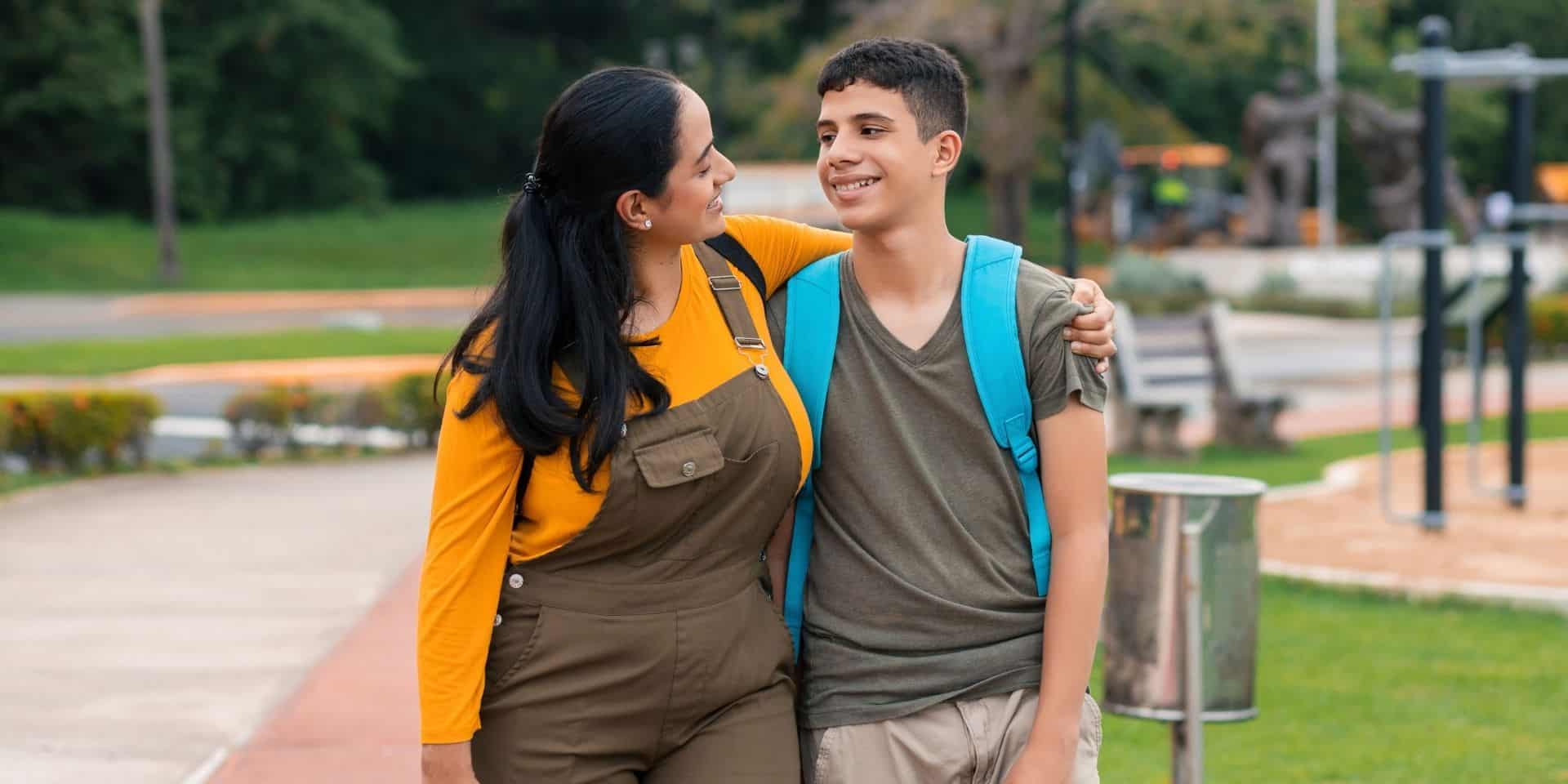 Mother and teenage son smiling at each other while walking in a park
