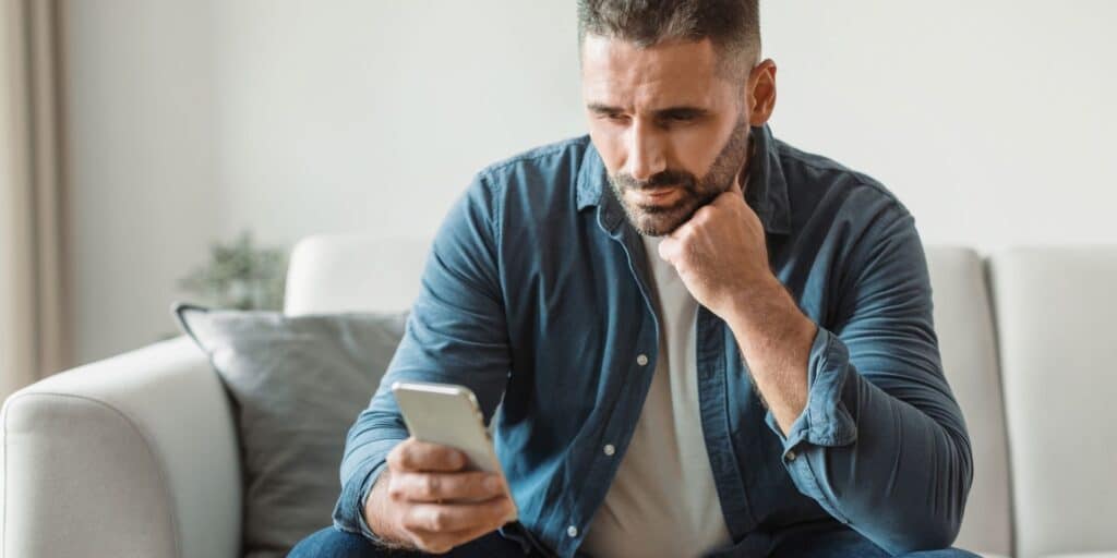 Thoughtful middle-aged man sitting on a couch looking at his phone