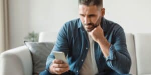 Thoughtful middle-aged man sitting on a couch looking at his phone