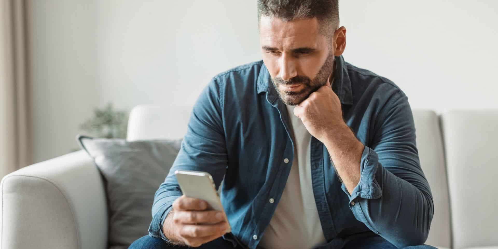 Thoughtful middle-aged man sitting on a couch looking at his phone