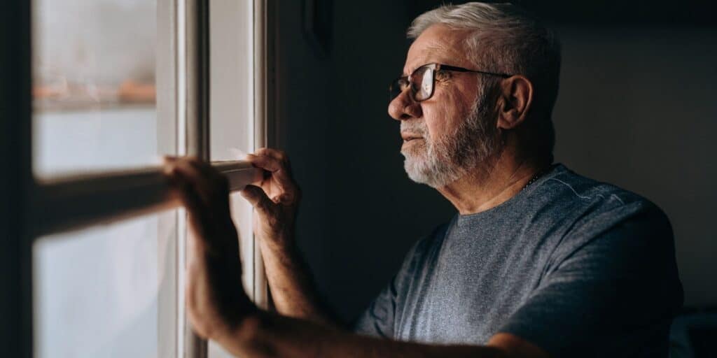 Older man with glasses looking out a window in quiet reflection