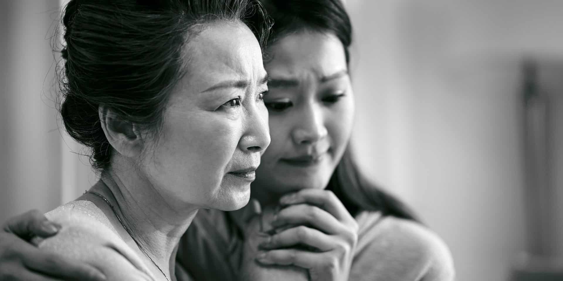 Grieving older woman being comforted by her adult daughter, in black and white